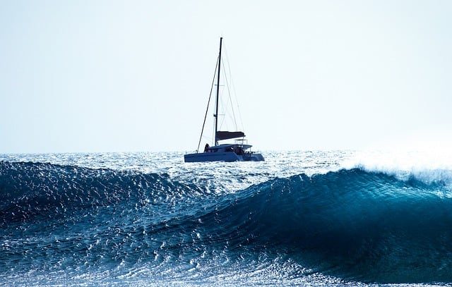 catamaran de voyage au mouillage derriere une vague, au fil de l'eau